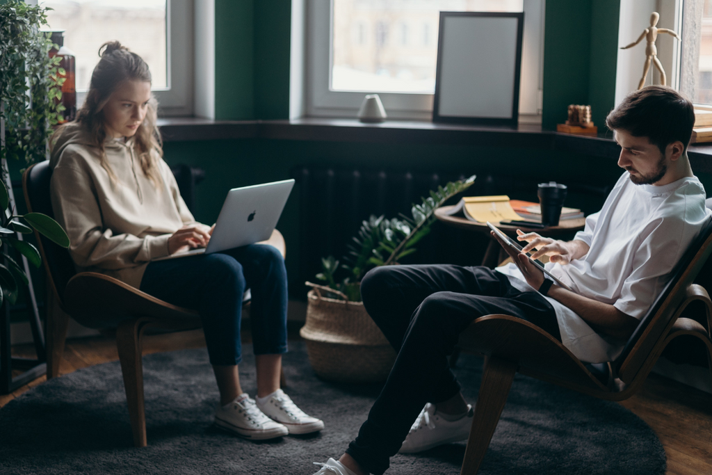 man and woman working together on their laptops, sitting down.