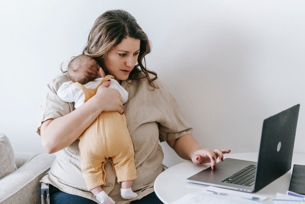 mum holding her baby whilst working on her laptop